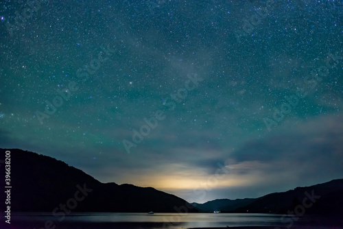 starry sky above the shape of mountains with the light of a city in a fjord in the Marlborough Sounds, New Zealand © ydumortier