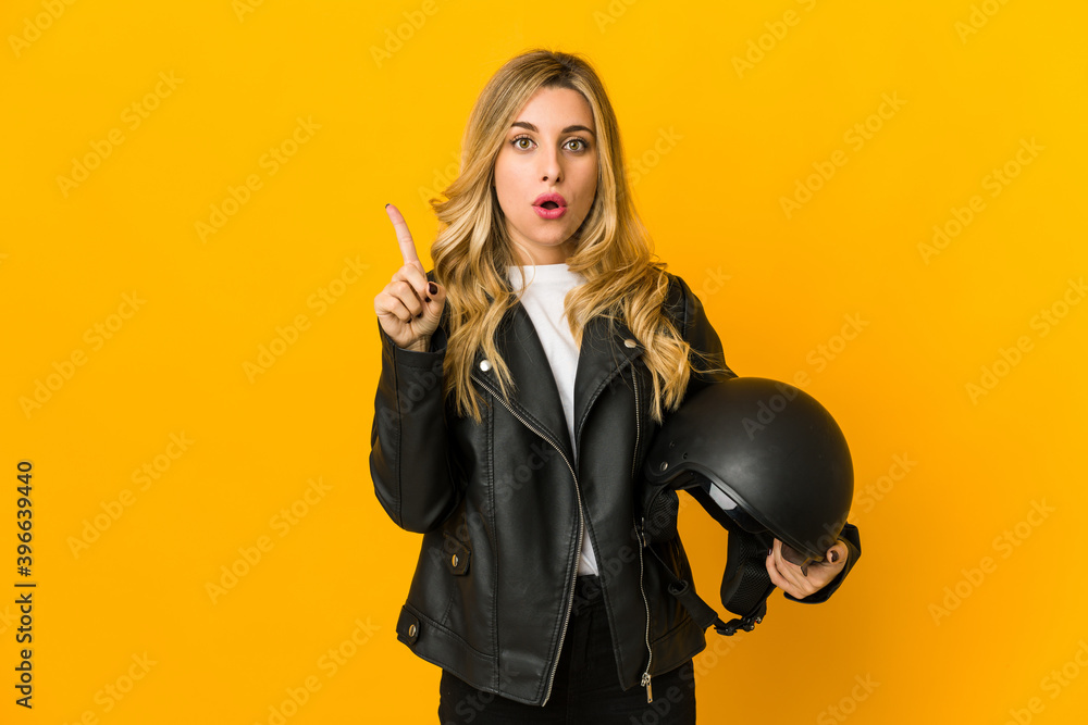 Young blonde caucasian biker woman holding helmet having some great idea, concept of creativity. Young blonde caucasian biker woman holding helmet having some great idea, concept of creativity.