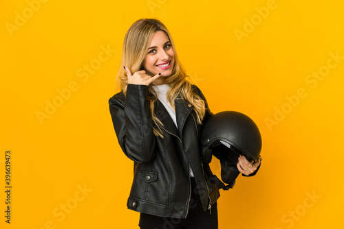 Young blonde caucasian biker woman holding helmet showing a mobile phone call gesture with fingers.