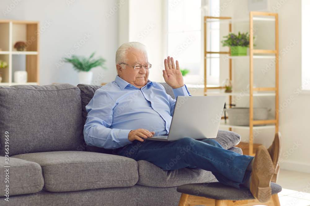 Happy smiling senior man sitting on sofa and talking on video call with family using laptop.