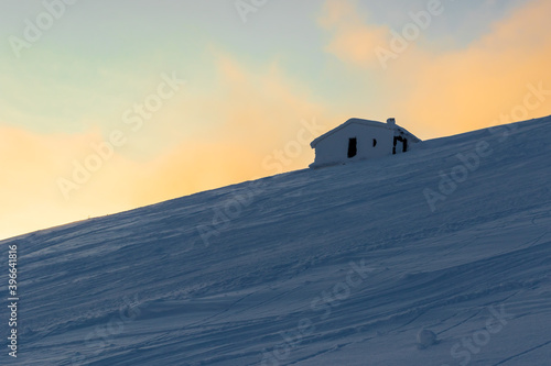 Evening landscape with a snow-covered house on a mountainside with a colorful sky in the background. Freeride. Powder.