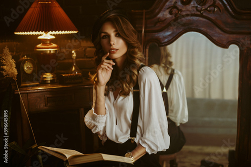 Elegant fashionable woman wearing  white shirt, black beret, suspenders, trousers, holding, reading book,  posing in beautiful dark interior. Copy, empty space for text