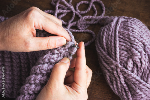 An adult woman holds knitting needles in her hands. Pale lilac thread color.