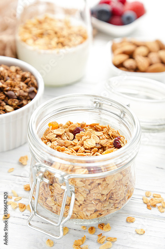 Tasty granola in glass jar and bowls on white wooden background