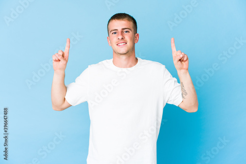 Young caucasian handsome man indicates with both fore fingers up showing a blank space.