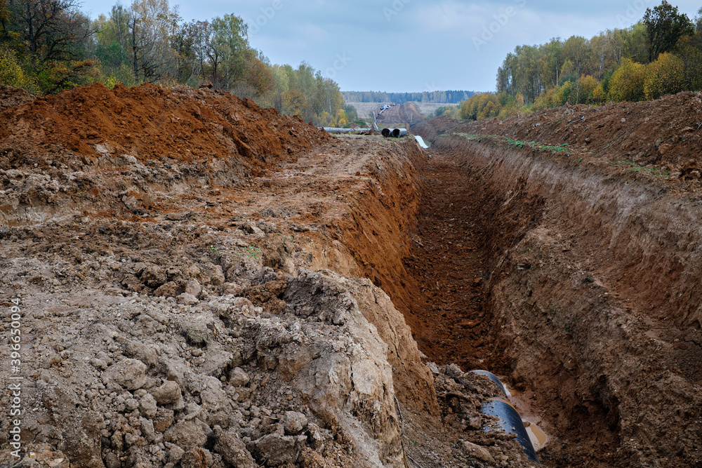 A dug trench, a pit for laying large-diameter pipes against the backdrop of an autumn forest. Construction of a gas pipeline or oil pipeline. A dug trench, a pit for laying large-diameter pipes against the backdrop of an autumn forest. Construction of a gas pipeline or oil pipeline.