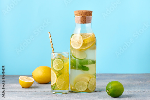 Fresh homemade lemonade with lime and mint in the glass with paper straw and bottle on bright blue background