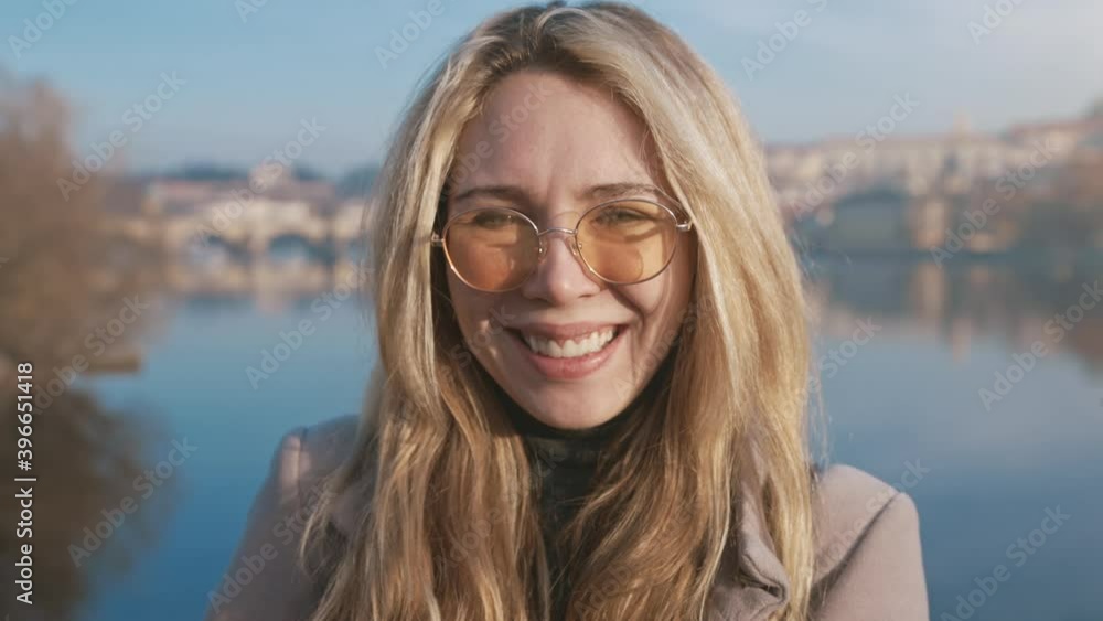 Closeup portrait of a happy young woman smiling at the camera. Natural blonde girl standing outside wearing sunglasses. Concept of beauty and happy lifestyle. Female model posing and looking straight Closeup portrait of a happy young woman smiling at the camera. Natural blonde girl standing outside wearing sunglasses. Concept of beauty and happy lifestyle. Female model posing and looking straight