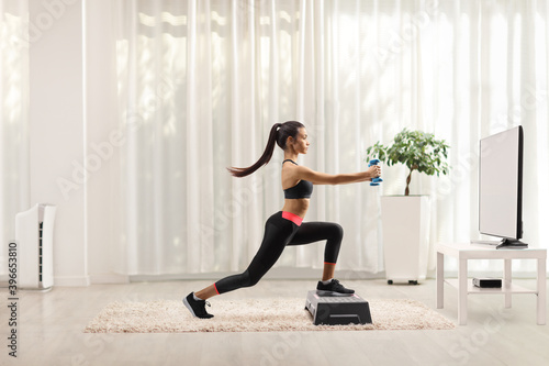 Female exercising step aerobic with small weights in front of a tv at home