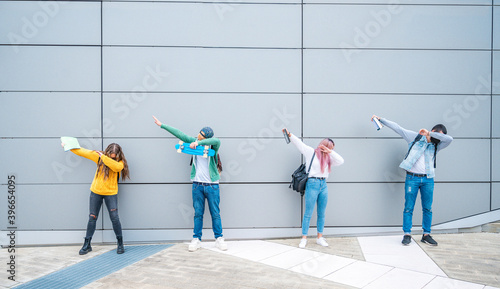 Happy multiracial teenage friends in casual clothes dancing dub dance on grey wall background after school.- New normal lifestyle concept with young students having fun together near to the campus