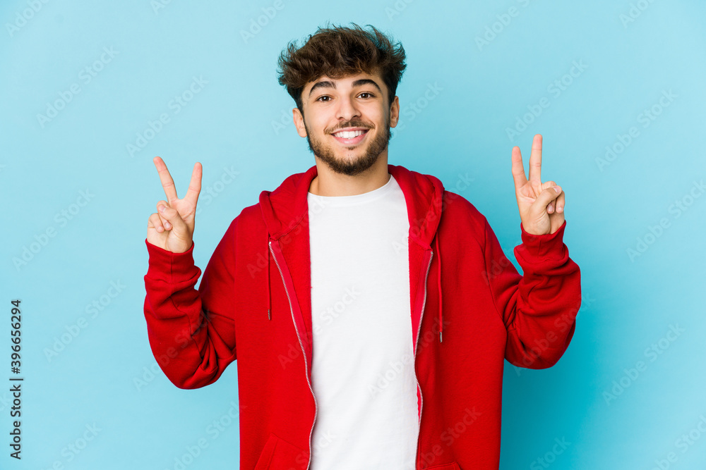Young arab man on blue background showing victory sign and smiling broadly. Young arab man on blue background showing victory sign and smiling broadly.