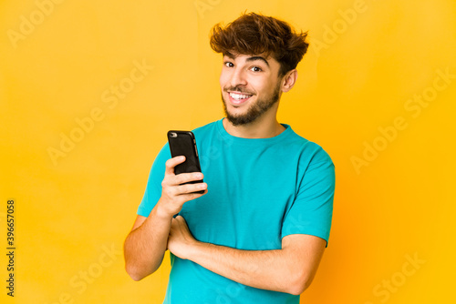 Young indian man holding a phone laughing and having fun. © Asier