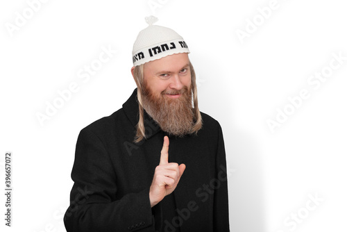 Obraz na płótnie Smiling bearded jewish man with sidelocks in white kippah hinting do not try to deceive me. Charismatic sly jew dressed in black coat showing warning with finger on white background. w salonie
