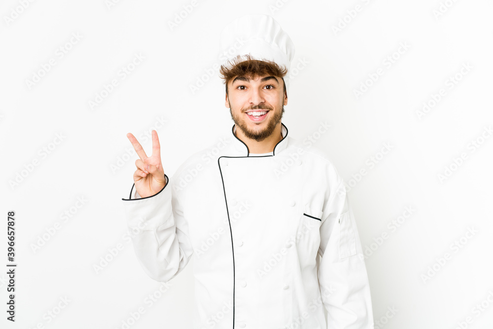 Young arab cook man joyful and carefree showing a peace symbol with fingers. Young arab cook man joyful and carefree showing a peace symbol with fingers.