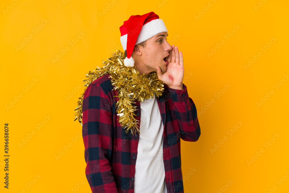 Young caucasian man with christmas hat holding a present isolated on yellow background Young caucasian man with christmas hat holding a present isolated on yellow background
