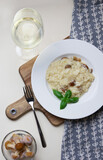 Vegetarian gourmet mushroom risotto on a white plate, yellow background, served with a glass of white wine. A northern Italian rice dish cooked with broth until it reaches a creamy consistency.