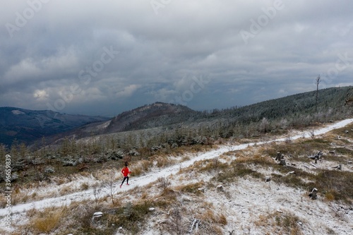 A drone view of a running woman athlete in a red sweatshirt on a mountain trail.