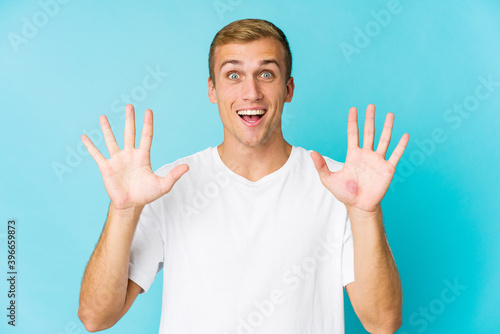 Young caucasian handsome man receiving a pleasant surprise, excited and raising hands.