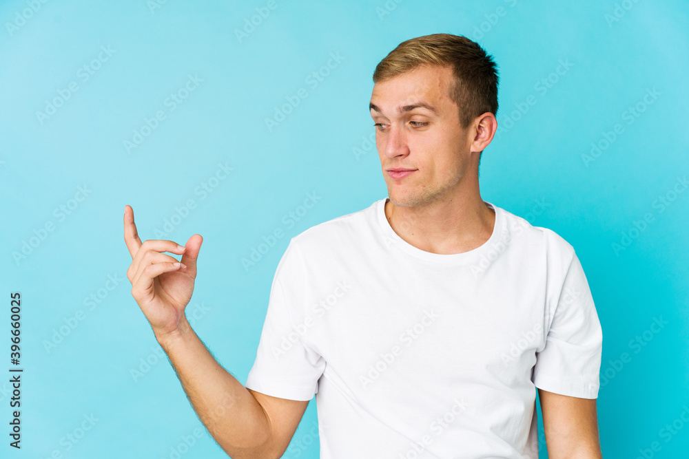 Young caucasian handsome man pointing with finger at you as if inviting come closer. Young caucasian handsome man pointing with finger at you as if inviting come closer.