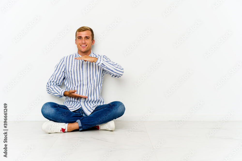 Young caucasian man sitting on the floor holding something with both hands, product presentation. Young caucasian man sitting on the floor holding something with both hands, product presentation.