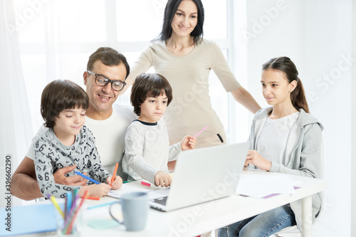Happy latin family with children spending time together at home. Father watching kids playing  drawing while working from home  using laptop
