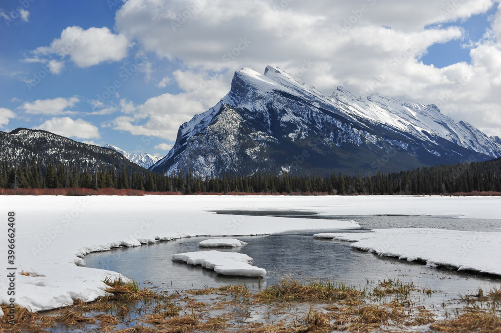 Melting snow covered waters of lake  in front of Snowy slopes of Mount Rundle in Banff National Park, Alberta Canada