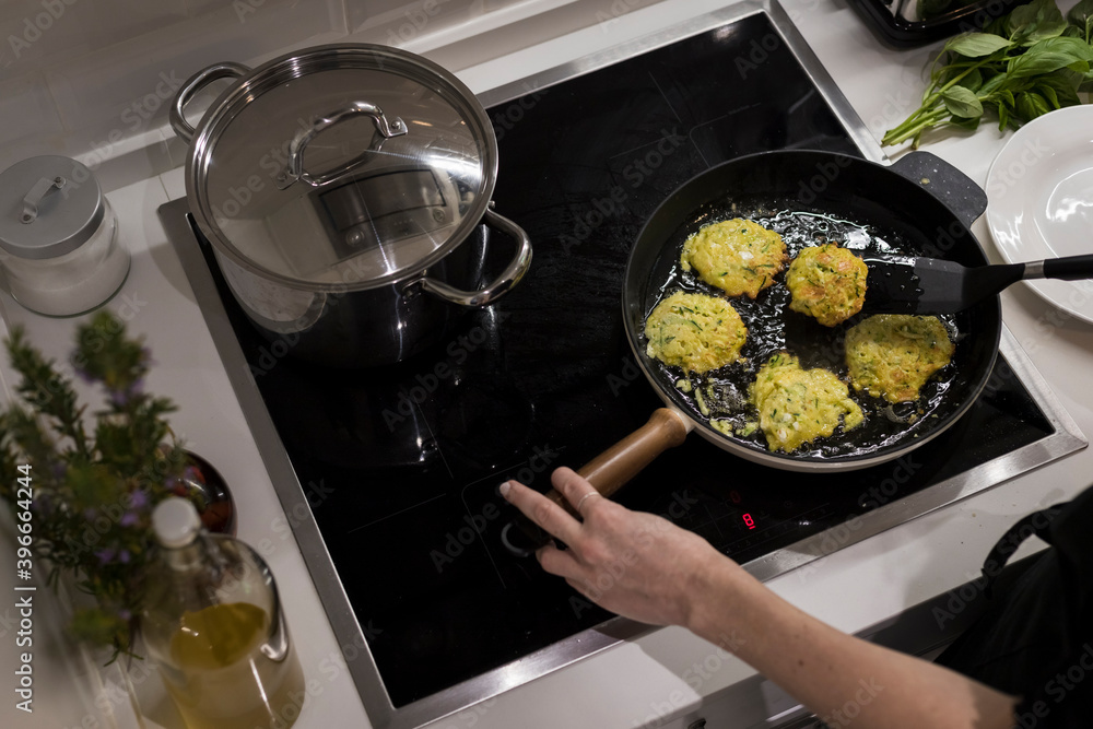 Young charming Swedish woman cooking at home in her kitchen, preparing healthy mediterranean food for her family. Young food blogger doing food preparation in her kitchen, frying vegetables