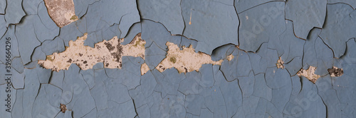 Peeling paint on the wall. Panorama of a concrete wall with old cracked flaking paint. Weathered rough painted surface with patterns of cracks and peeling. Panoramic texture for background and design.