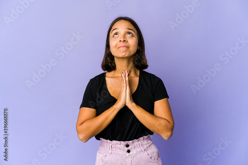 Young mixed race woman holding hands in pray near mouth, feels confident.