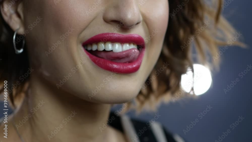 A beautiful girl model with red lipstick runs her tongue over her teeth, smiling broadly close up shooting. Cute young girl posing in a photo studio. A beautiful girl model with red lipstick runs her tongue over her teeth, smiling broadly close up shooting. Cute young girl posing in a photo studio.