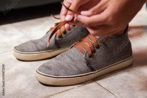 Detail of the hands of a young Brazilian man tying the tennis shoe to practice walking in the neighborhood. Footwear concept. Sport concept.