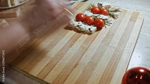 Flat lay of cheese and tomatoes. Hands arranging slices of cheese, tomatoes and rozmarin in a shape of Christmas Tree. Food for Christmas holiday. Timelapse photo