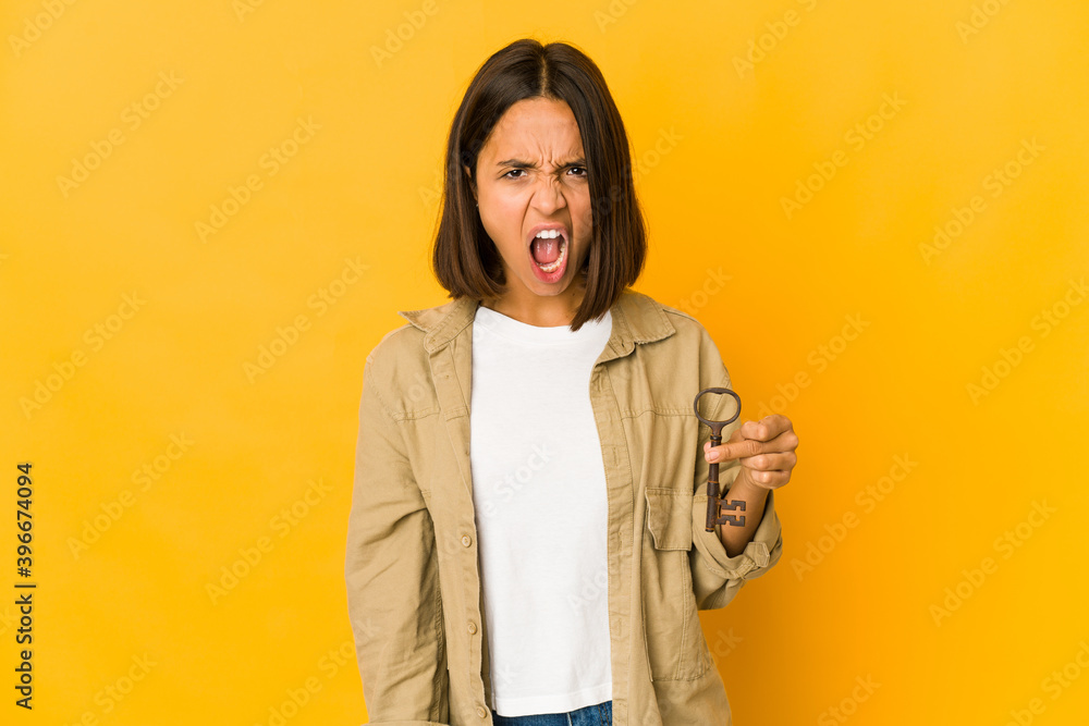 Obraz premium Young hispanic woman holding an old key screaming very angry and aggressive.