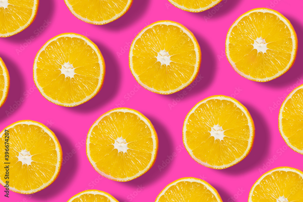 Top down view on pink abstract background with slices of ripe orange or lemon citrus in pattern - trendy minimal flat lay food summer concept