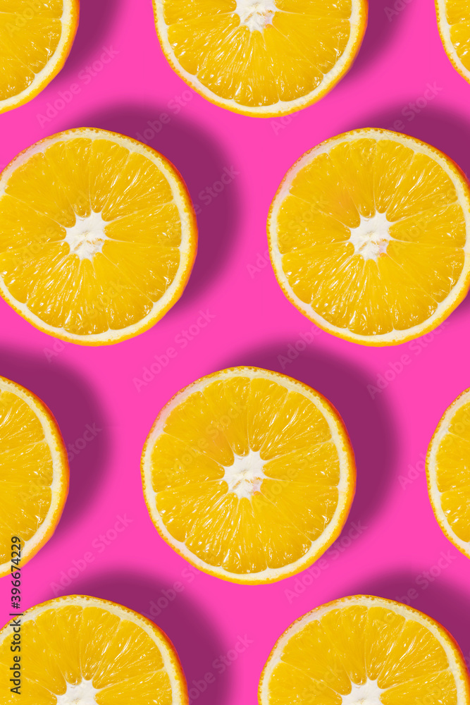 Top down view on pink abstract background with slices of ripe orange or lemon citrus in pattern - trendy minimal flat lay food summer concept