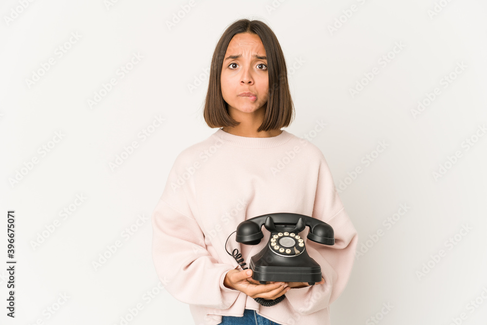 Young hispanic woman holding a vintage telephone isolated confused, feels doubtful and unsure.
