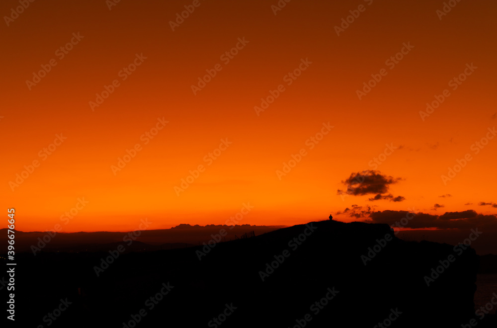 orange sunset with mountain silhouette and a person