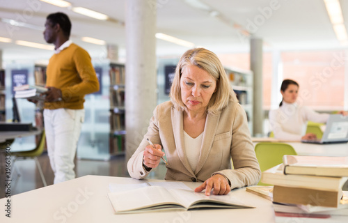 Elderly woman makes notes in notebook and read book in public library. High quality photo