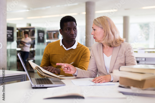 Female teacher working with african-american man in university library. High quality photo
