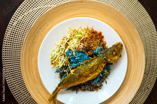 Nasi kerabu is a Malay rice dish, a type of nasi ulam, in blue-coloured and eaten either with fried fish, fried chicken. Served with fish crackers, salted egg, pickles, budu and other salads. photo