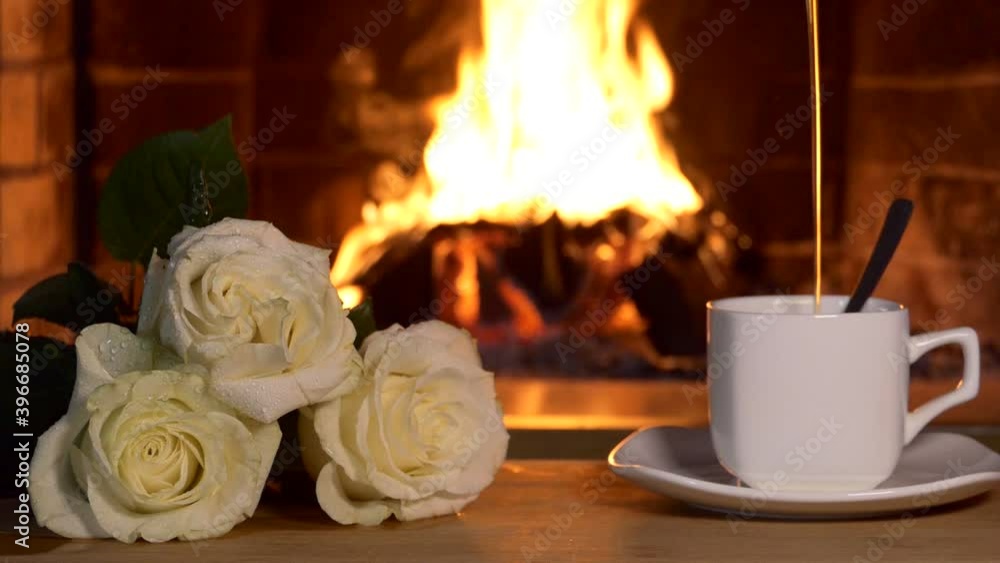 Slow motion, Fireplace. Roses and a tea Cup in which a thin stream of tea is poured against the background of the fireplace flame. Close-up shooting. Slow motion, Fireplace. Roses and a tea Cup in which a thin stream of tea is poured against the background of the fireplace flame. Close-up shooting.