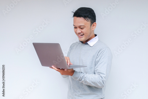 Young Asian man feeling happy and smile when standing and work laptop. Indonesian man wearing grey shirt