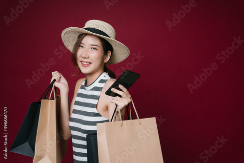 Portrait of asian woman enjoy online shopping with smartphone and holding paper bags.
