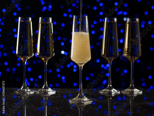 A glass glass is filled with sparkling wine against the background of four poured glasses.