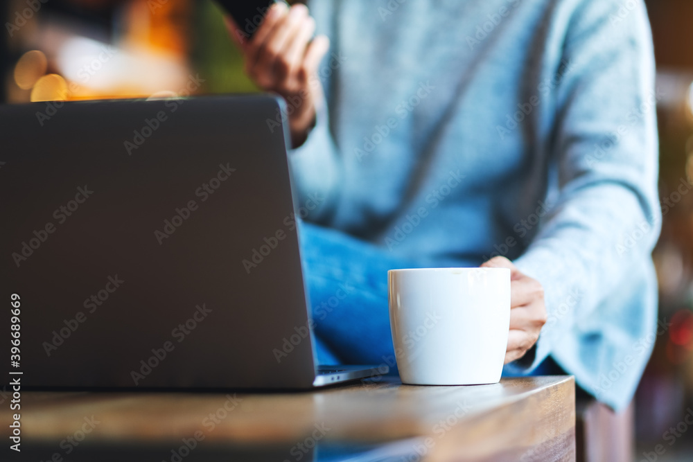 Closeup image of a woman holding and using mobile phone and laptop computer while drinking coffee Closeup image of a woman holding and using mobile phone and laptop computer while drinking coffee