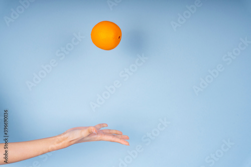 Woman hand throwing an orange up in the air isolate on blue background.