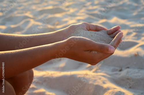 Young woman holds sand in her hands, at sunset