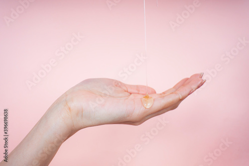 Woman hand with liquid oil lotion cream pouring from top screen.