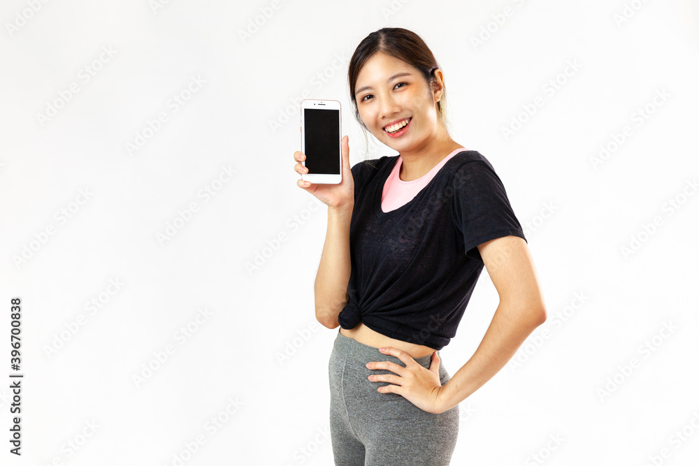 Asian woman wearing exercise clothes smiling at camera holding cell phone white background