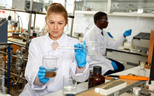 Focused woman lab technicians in glasses working with reagents and test tubes  man on background